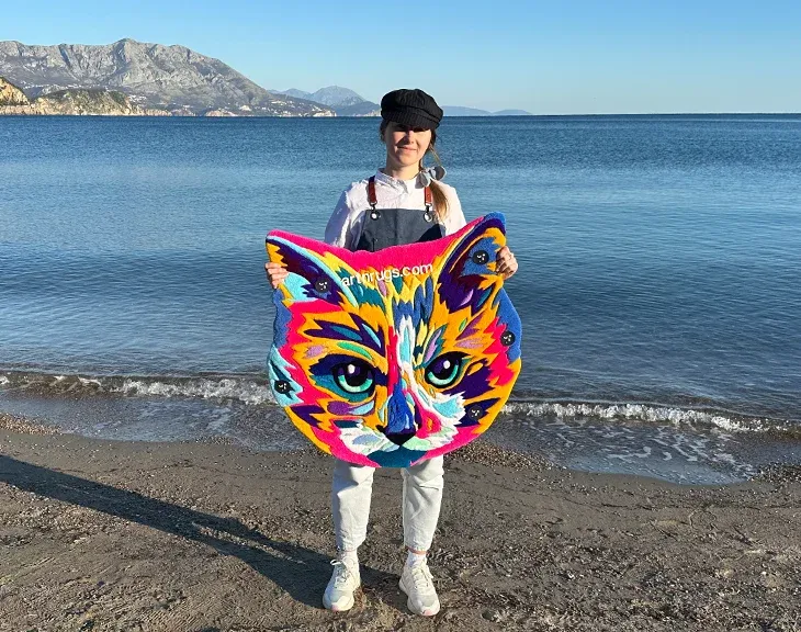 Person holding the multicolor cat portrait rug by the sea.
