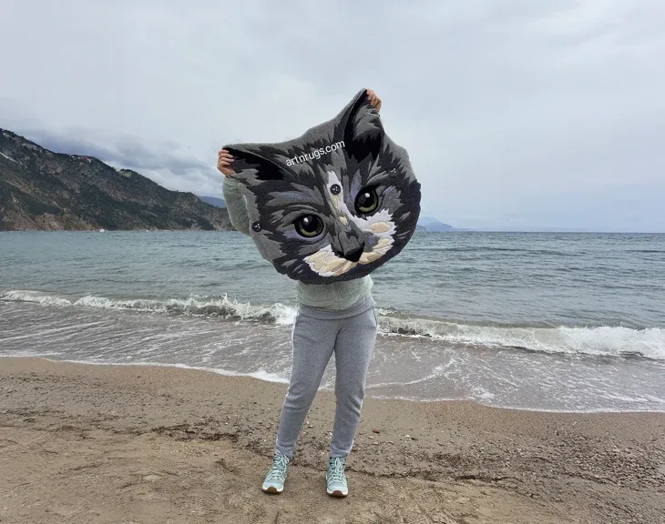 Kseniia Derr holding the gray cat portrait rug by the sea.