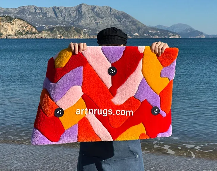 Person holding the red and orange parquet rug by the sea.