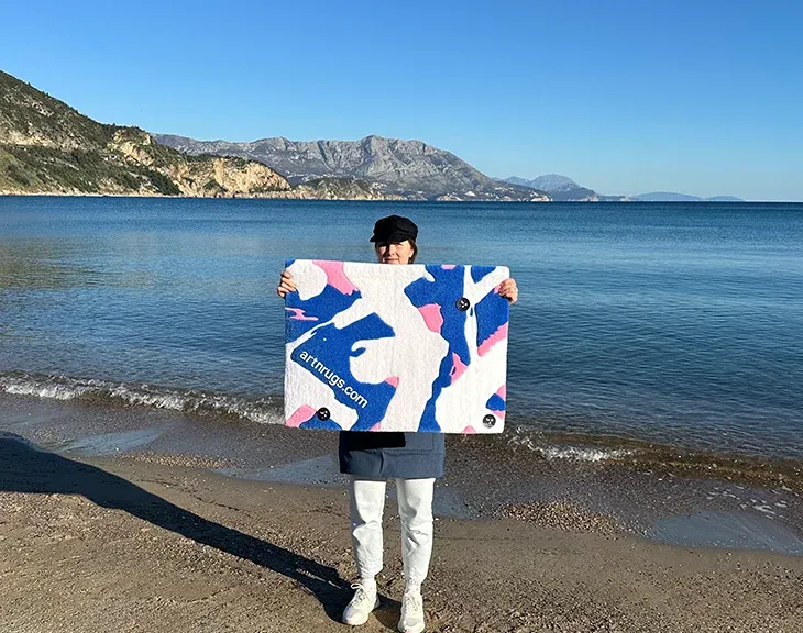 Ksenia Derr presenting her custom blue white pink abstract rug against seaside view