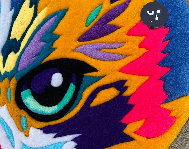 Person holding the multicolor cat portrait rug on the beach.