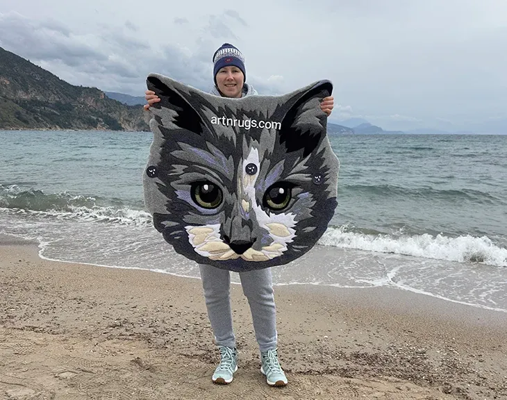 Kseniia Derr holding the gray cat portrait rug on the beach.