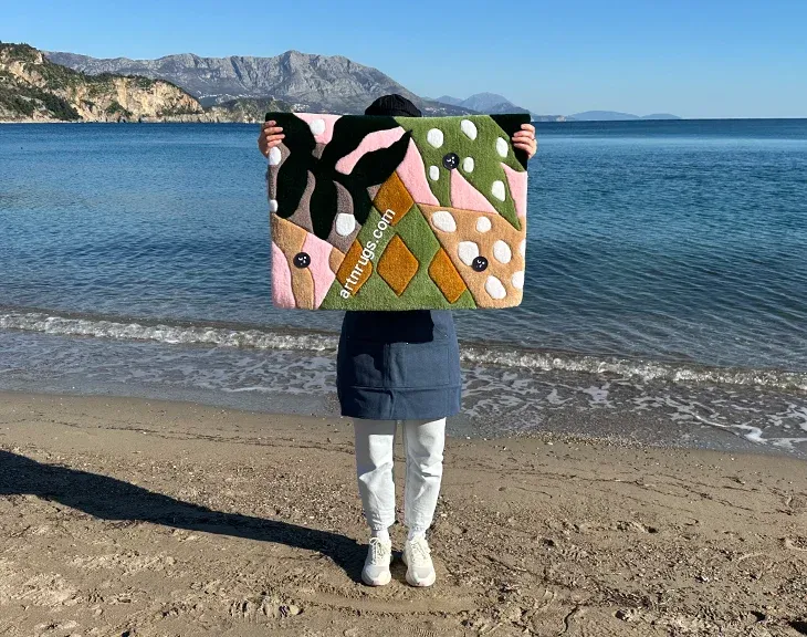 Person holding the tropical leaf rug on a beach with sea and mountains behind.