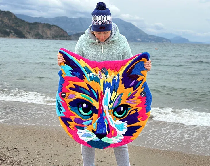 Angled view of the multicolor cat portrait rug on sand.