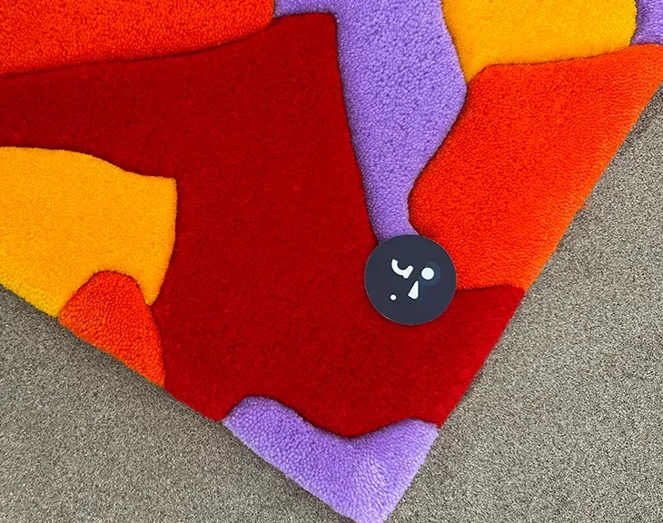 Close-up of dense sheared acrylic pile on a hand-tufted rug, with clean carved edges between red, orange and purple colour fields