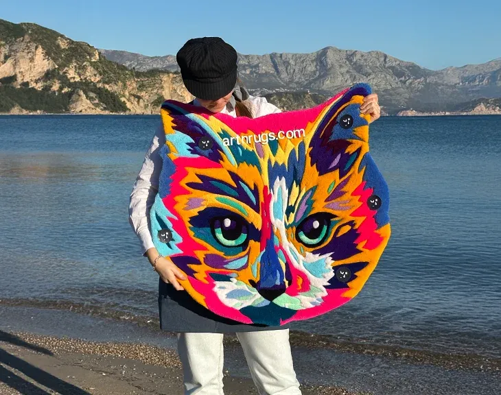 Kseniia Derr holding a finished hand-tufted cat portrait rug by the sea