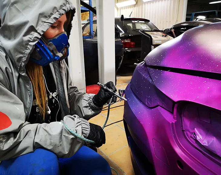 Kseniia Derr airbrushing a car in a purple and magenta finish
